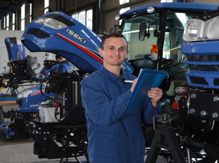 Ein Mitarbeiter der Iseki Werkstatt in blauer Uniform hält ein Klemmbrett in der Hand