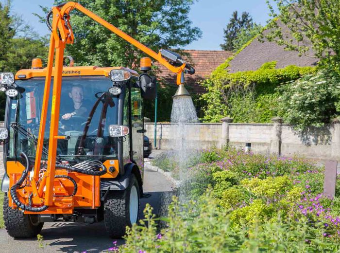 Ein Multihog-Giessarm-Traktor sprüht Wasser auf eine Straße zur Staubbindung und Straßenpflege