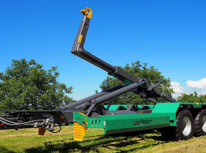 Grüner Traktor mit Kran, ausgestattet mit einem Oehler THK130 Anhänger, auf einem Feld im Einsatz