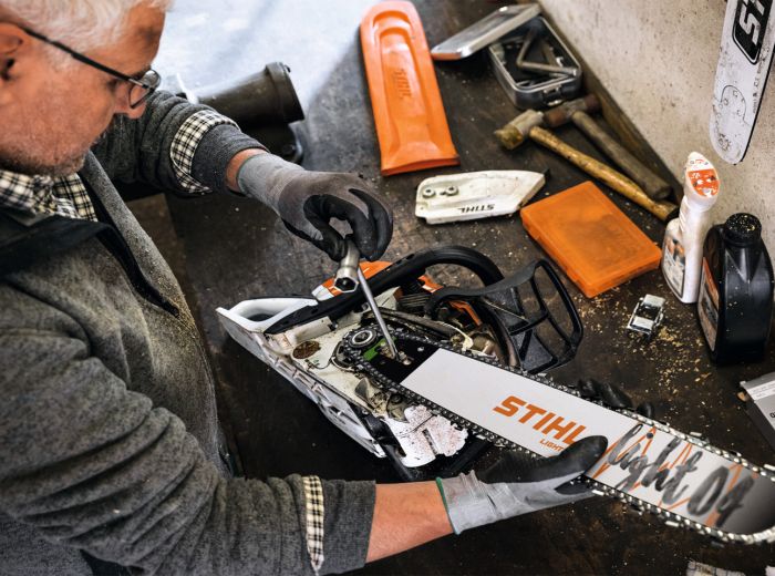 Ein Mann repariert eine Stihl Kettensäge in seiner Werkstatt, umgeben von Werkzeugen und Materialien