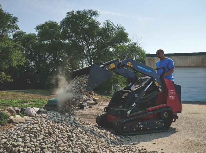 Ein Mann nutzt den Toro Dingo TX1000, einen roten und schwarzen Mini-Bagger, um Kies zu transportieren